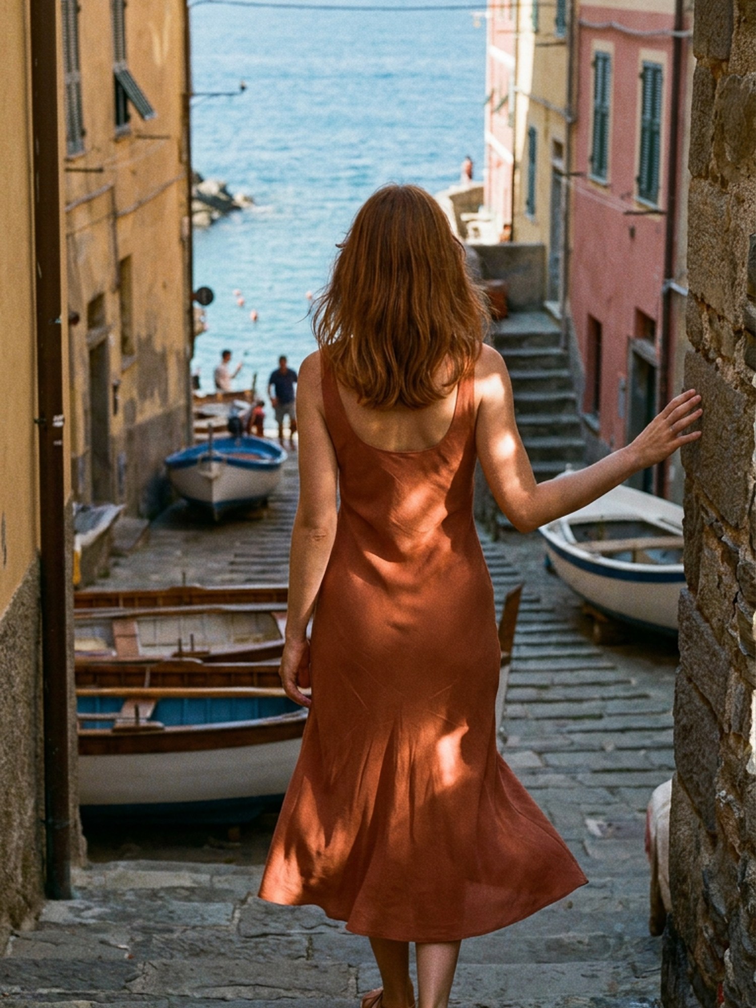 Terracotta bias-cut linen dress descending stone steps toward the fishing boats at Vernazza